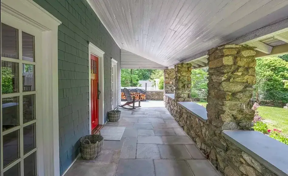 Covered porch with a stone wall and a red painted door